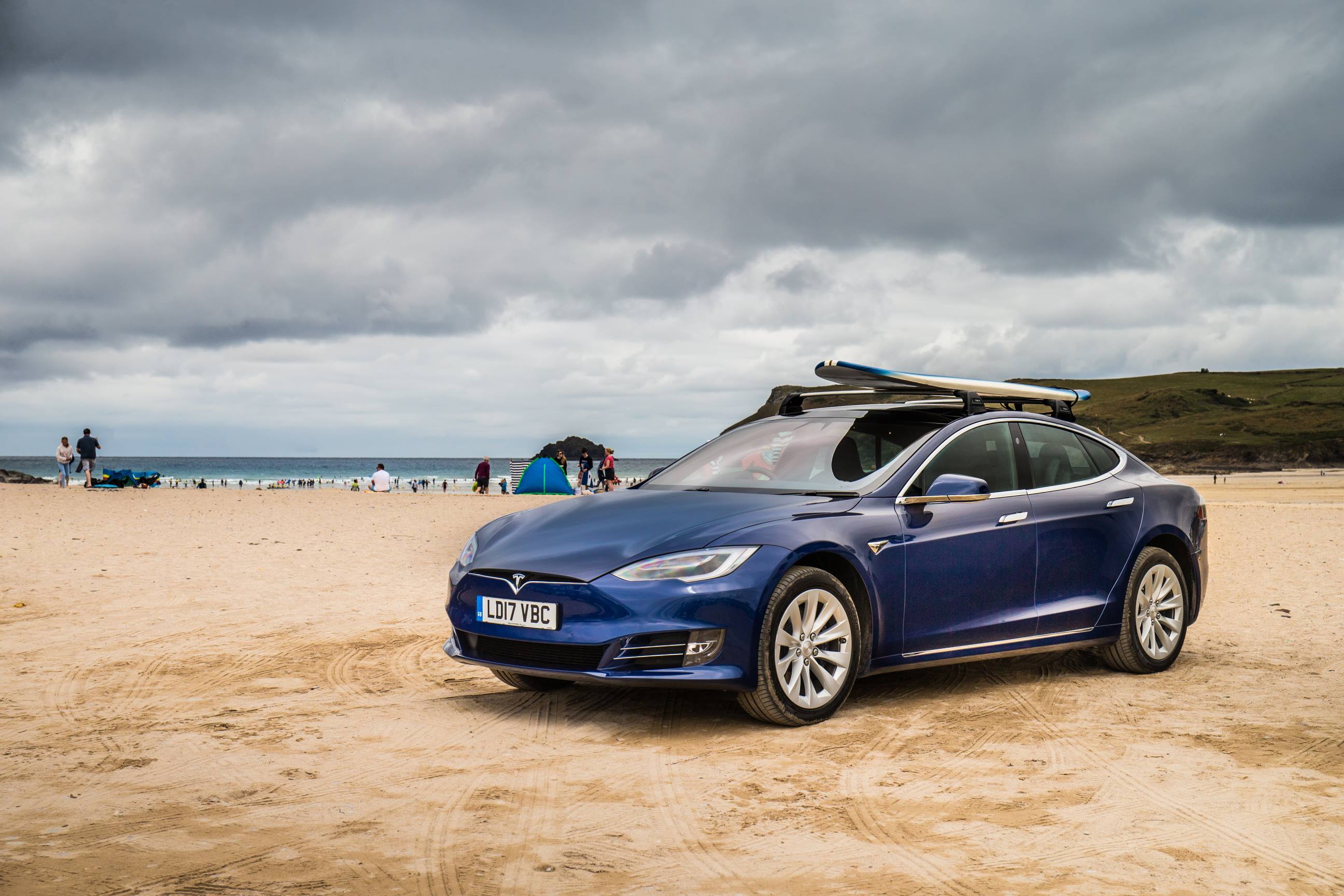 Blue Tesla Model S on beach with surfboard on roof